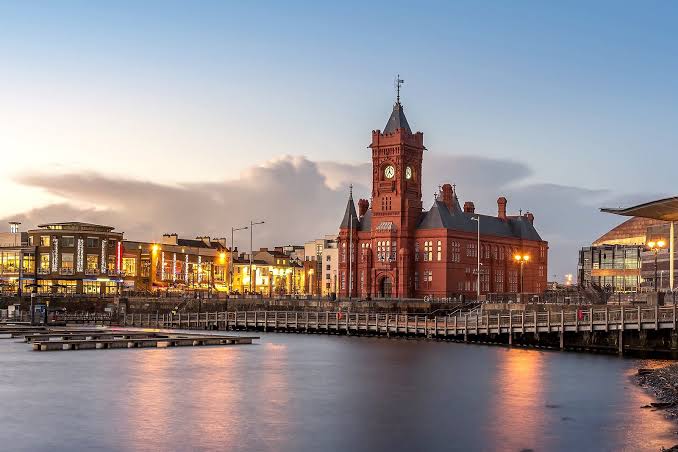 Cardiff Bay at dusk with the red-brick Pierhead Building, waterfront bars and the Senedd reflected in the water