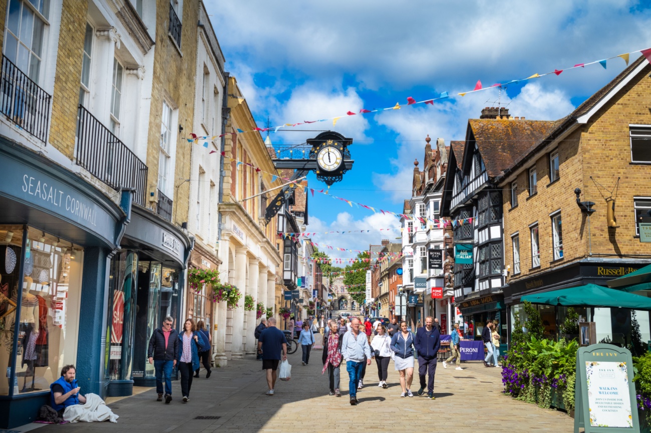 Shoppers on Winchester High Street beneath the ornate City Cross clock and bunting