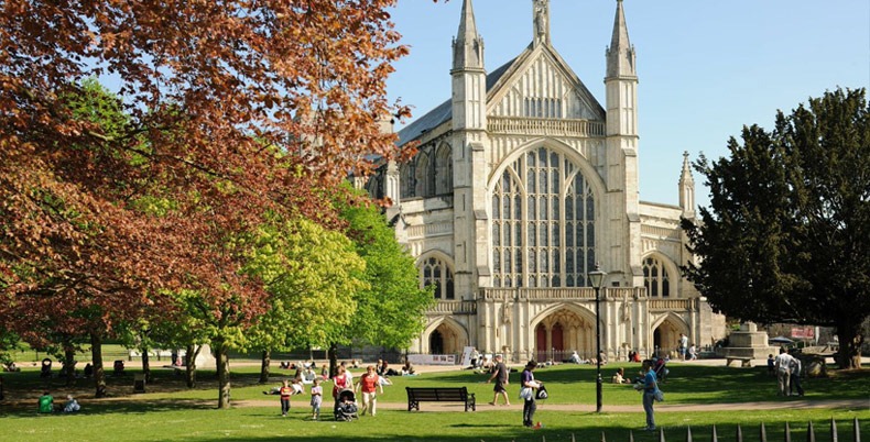 Winchester Cathedral seen across the green with trees and visitors
